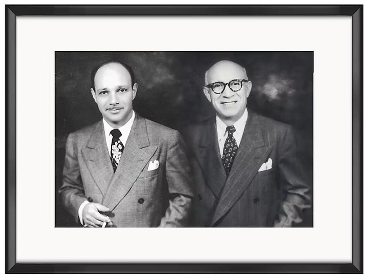 Black and white photograph of two men in suits and ties, framed with a black border.